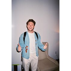 a man is standing in front of a chair and giving the thumbs up sign with both hands