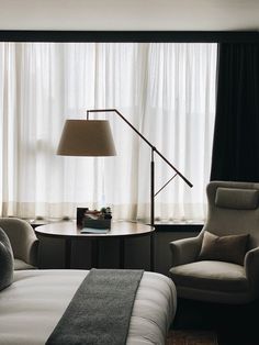 a bedroom with a bed, chair and lamp in front of a window that has curtains