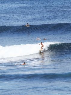 three surfers are riding the waves in the ocean, one is surfing and another is swimming