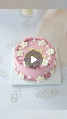 a pink cake with white flowers on it and a video player in the background looking at it