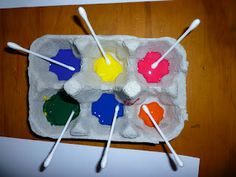 an egg carton filled with different colored paint and marshmallows on sticks