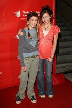 two young women standing next to each other on a red carpet