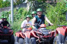 people riding four wheelers on the road with green helmets and trees in the background