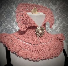 a pink crocheted shawl with buttons and pearls on the collar is hanging from a mannequin's dummy