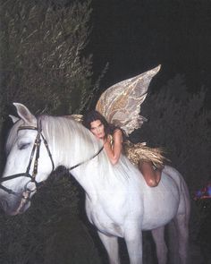 a woman sitting on the back of a white horse next to a forest at night