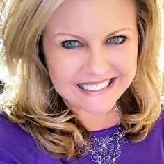 a woman with blonde hair and blue eyes wearing a purple shirt smiling at the camera