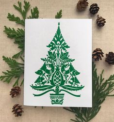 a card with a green christmas tree on it next to pine cones and evergreen needles