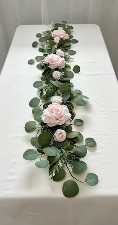 a long table with flowers and greenery on the top, along with green leaves