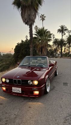 a red car parked on the side of a road next to trees and palm trees