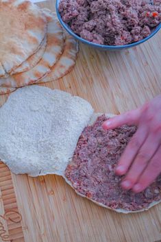 a person is kneading ground meat on top of pita bread