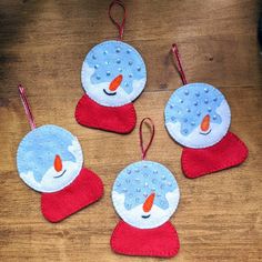 four snowman ornaments are hanging on a wooden table with red and blue felts