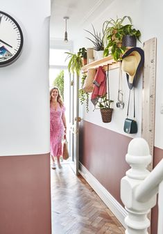 a woman in a pink dress is walking down the hall way with plants on the wall