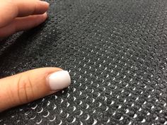 a woman's hand with white nail polish on top of a black cloth covered in circles