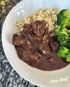 a white bowl filled with beef and rice next to broccoli on a table