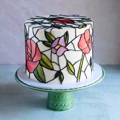 a white cake with pink flowers on it sitting on top of a green pedestal next to a wall