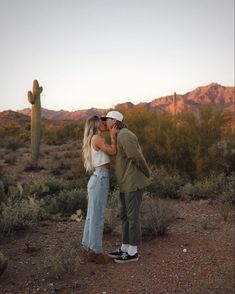 a man and woman kissing in front of a saguado with mountains behind them