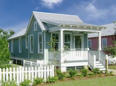 a white picket fence surrounding a small blue and pink house with a porch on the second floor