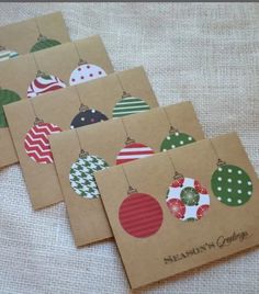 four christmas cards with ornaments on them sitting on a white cloth covered tablecloth, one is brown and the other is green