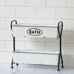 a bathroom shelf with a bath sign on the bottom and two shelves below it, against a white tiled wall