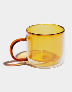 a yellow glass cup sitting on top of a white table next to a brown handle