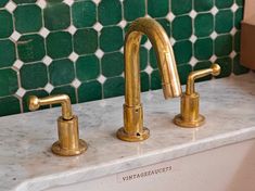 two brass faucets on a marble countertop in a green tile backsplash