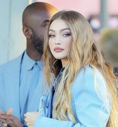 a woman with long blonde hair standing next to a man in a blue shirt and jeans