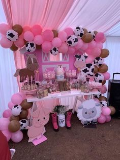 a table topped with lots of pink and brown balloons next to a cow themed cake