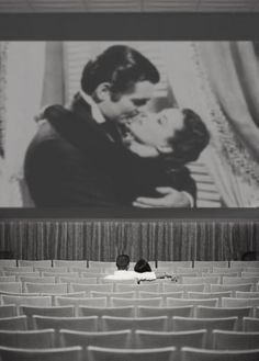 two people are kissing in front of a large screen with the image of a man and woman on it