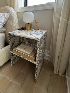 a small table with books on it in front of a window and a white chair