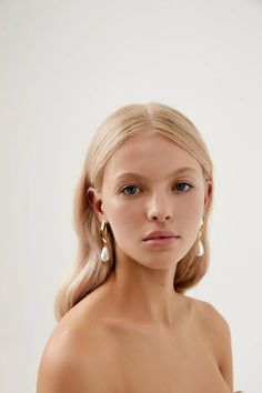 a woman with blonde hair and blue eyes is wearing gold earrings in front of a white background