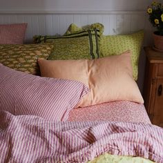 an unmade bed with pink and green sheets, pillows and flowers on the headboard