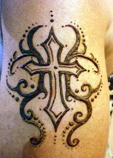 a cross tattoo on the side of a woman's leg, with swirls and dots