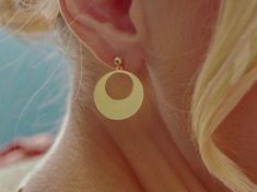 a close up of a woman's ear wearing gold earrings with an oval design