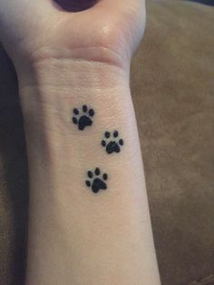 a person with a small wrist tattoo that has two dogs paw prints on the wrist