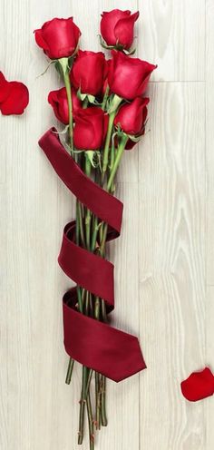 a bunch of red roses with a ribbon tied around them on a white wooden surface