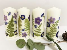 three white candles with purple flowers and green leaves