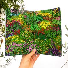 a hand holding up an art piece with flowers and plants painted on the inside of it