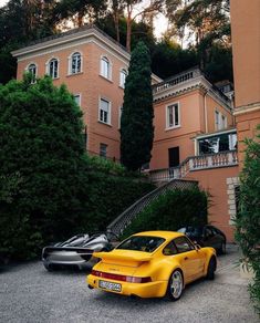 two yellow sports cars parked in front of a large pink building with stairs leading up to it