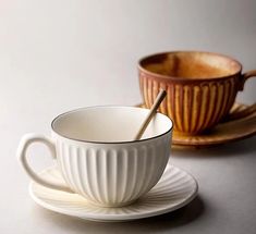 two cups and saucers on a white surface with one cup in the middle, another empty