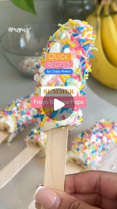 a person holding a popsicle with sprinkles on it and bananas in the background