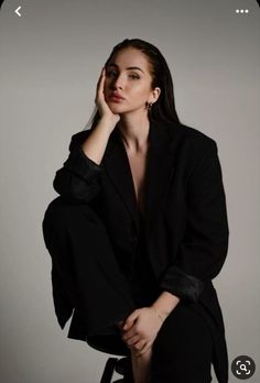 a woman sitting on top of a chair wearing a black suit