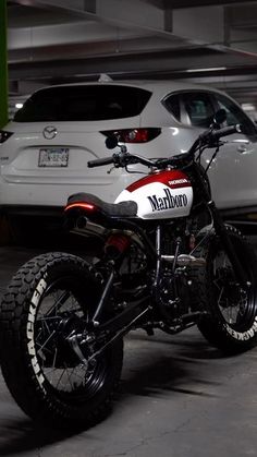 a red and white motorcycle parked in a parking garage next to a white car on the street