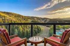 two wooden chairs sitting on top of a balcony next to a forest filled mountain range