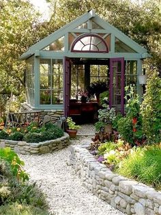 a garden shed with lots of plants and flowers in the front, along with gravel path leading up to it