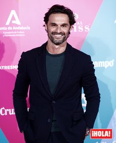 a man standing in front of a pink and blue background wearing a black blazer