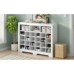 a white bookcase with many compartments and baskets on the bottom shelf next to a potted plant