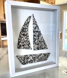 a sailboat made out of shells in a white frame