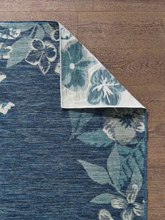 a blue area rug with flowers on it and a white border around the edge that is laying on a wooden floor