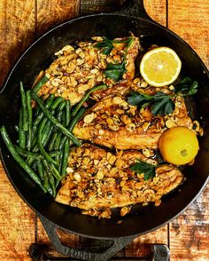 a skillet filled with chicken, green beans and lemons on top of a wooden table