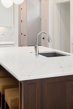 a white kitchen with marble counter tops and stools next to an island in the middle